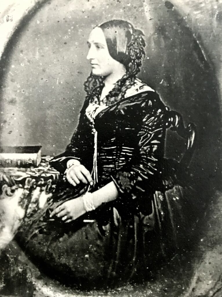 A woman sitting in a long black dress, facing to the left. 