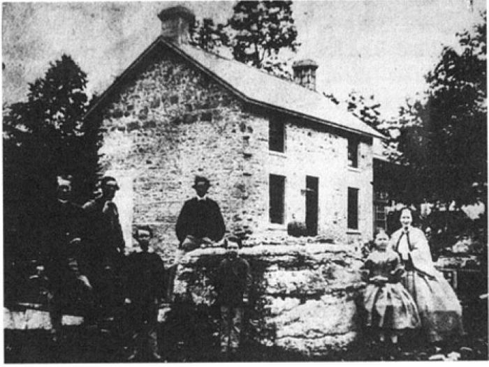 an old mill with five people (three men and two women) standing in front of it