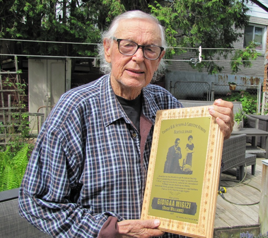A white haired man with glasses (Douglas Williams) holding a plaque. 
